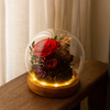 Decorative glass globe with preserved flowers on a wooden base, illuminated from below.