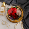 Glass dome with preserved roses, perfume bottle, earrings, and pearl necklace on a marble surface.