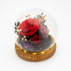 Glass dome with preserved red and purple roses on a wooden base against a white background