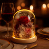 Decorative glass dome with flowers on a romantic dinner table with wine and plates.