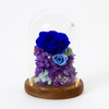 Decorative floral arrangement with blue and purple preserved flowers under a glass dome on a wooden base.