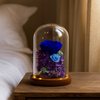 Decorative glass dome with blue and purple preserved flowers on a wooden surface.