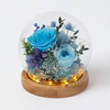 Decorative glass sphere with blue preserved flowers on a wooden base against a white background