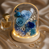 Decorative display with blue roses under a glass dome on a beige fabric background.
