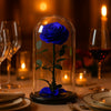 Blue rose under a glass dome on a dinner table with wine glasses and candles.