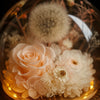 Decorative arrangement of preserved flowers and a dandelion in a glass container with warm lighting.