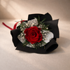 Bouquet with a red preserved rose, black ribbon, and greenery on a beige background