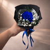 Bouquet with a blue preserved rose held by a hand against a neutral background