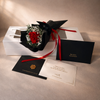 Bouquet of red preserved rose with black ribbon, card, and envelope on a beige surface