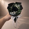 Bouquet with black preserved rose and greenery held by a hand against a neutral background
