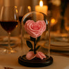 Pink rose in a glass dome on a romantic dinner table with candles and wine glasses.