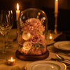 Decorative glass dome with flowers on a table setting with candles and cutlery.