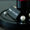Black preserved carnation dome base with 'Mom I love you' text on a reflective surface with pearls.