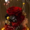 Bouquet of red preserved roses and other flowers under a glass dome with warm lighting.