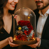 Two people holding a glass dome with a bouquet of preserved flowers inside, smiling.