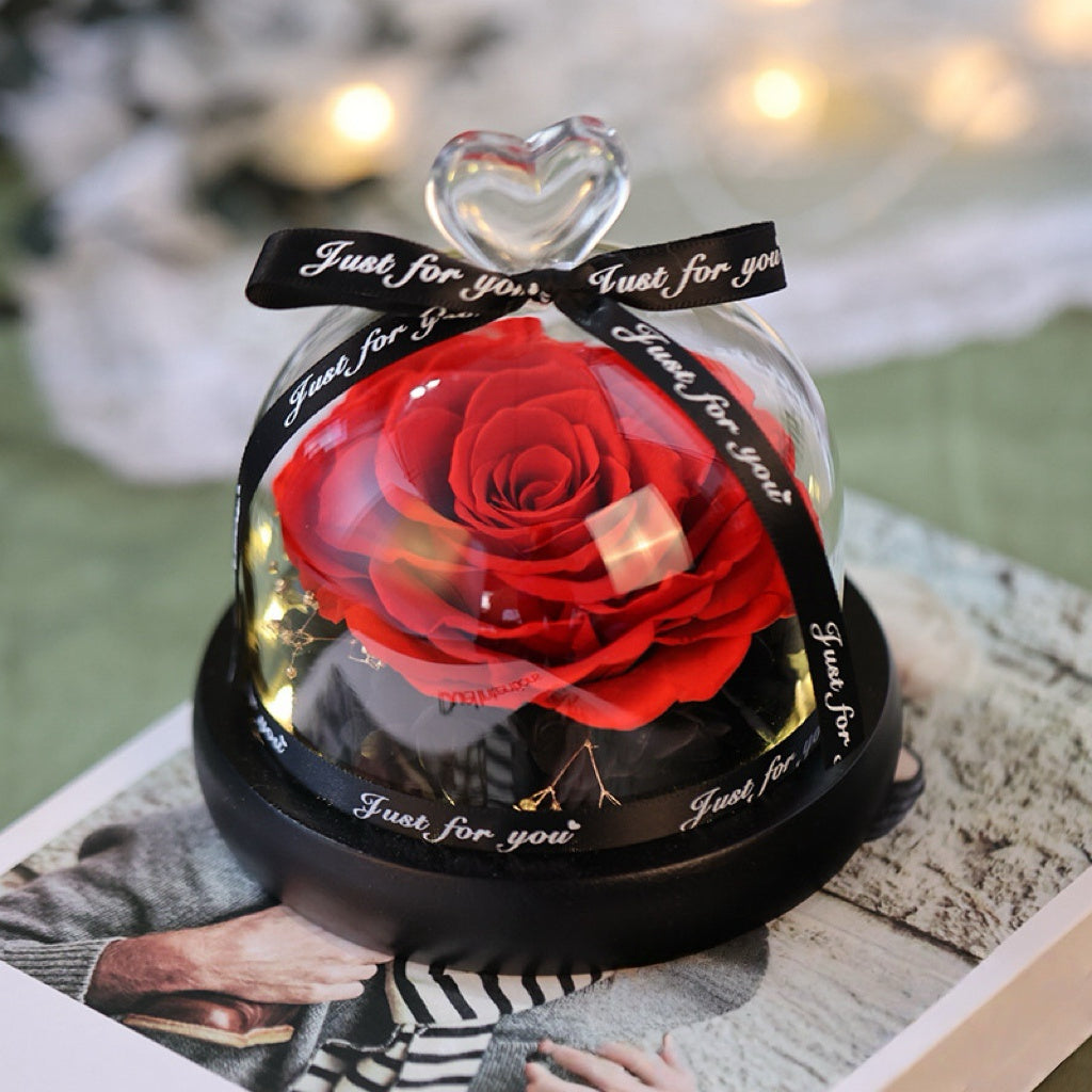 Red preserved rose in a glass dome with a black heart-shaped ribbon on a blurred background