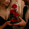 Two people holding a glass dome with red roses inside.