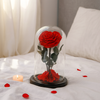 Red rose inside a glass dome on a soft surface with scattered petals and a candle.