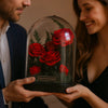 Two people holding a glass dome with preserved red roses.