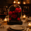 Decorative display of preserved red roses under a glass dome on a romantic dinner table with candles and wine glasses.