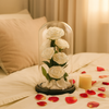 White preserved roses in a glass dome on a bed with red rose petals