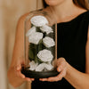 Person holding a glass dome with white roses inside